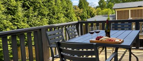 Terraza al aire libre con una mesa dispuesta para dos personas, que incluye una botella de vino, copas y una tabla con queso y uvas.