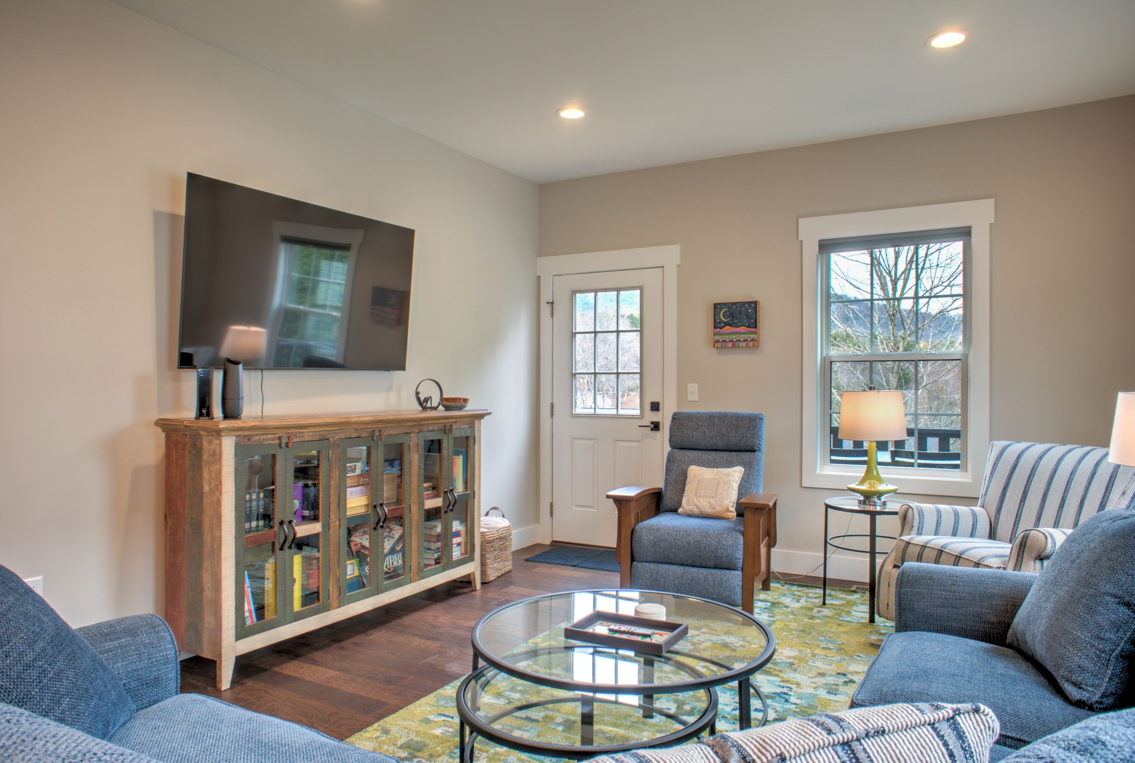 A living room with a glass coffee table, blue sofas, a wooden cabinet, and a television on the wall.