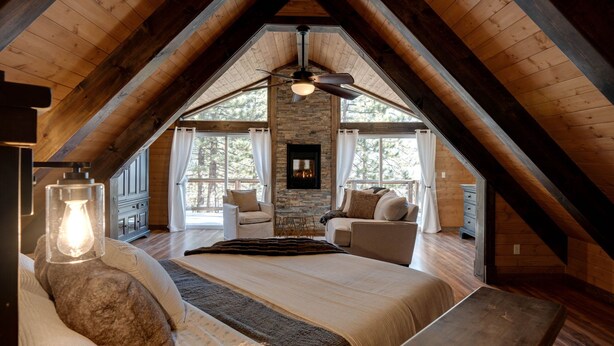A cozy attic bedroom with a stone fireplace, wooden beams, and a large bed.