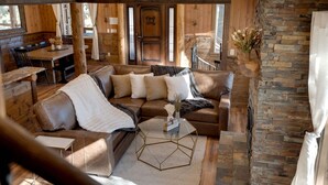 A cozy living room with a brown leather sofa, a glass coffee table, and a stone wall.