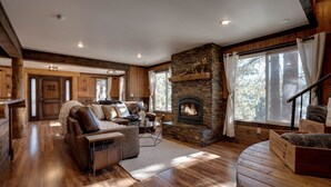 A cozy living room with a stone fireplace, wooden floors, and a large window.