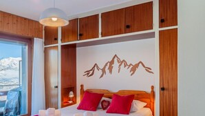Habitación de hotel con cama, paneles de madera, un mural de montañas y vistas al exterior.