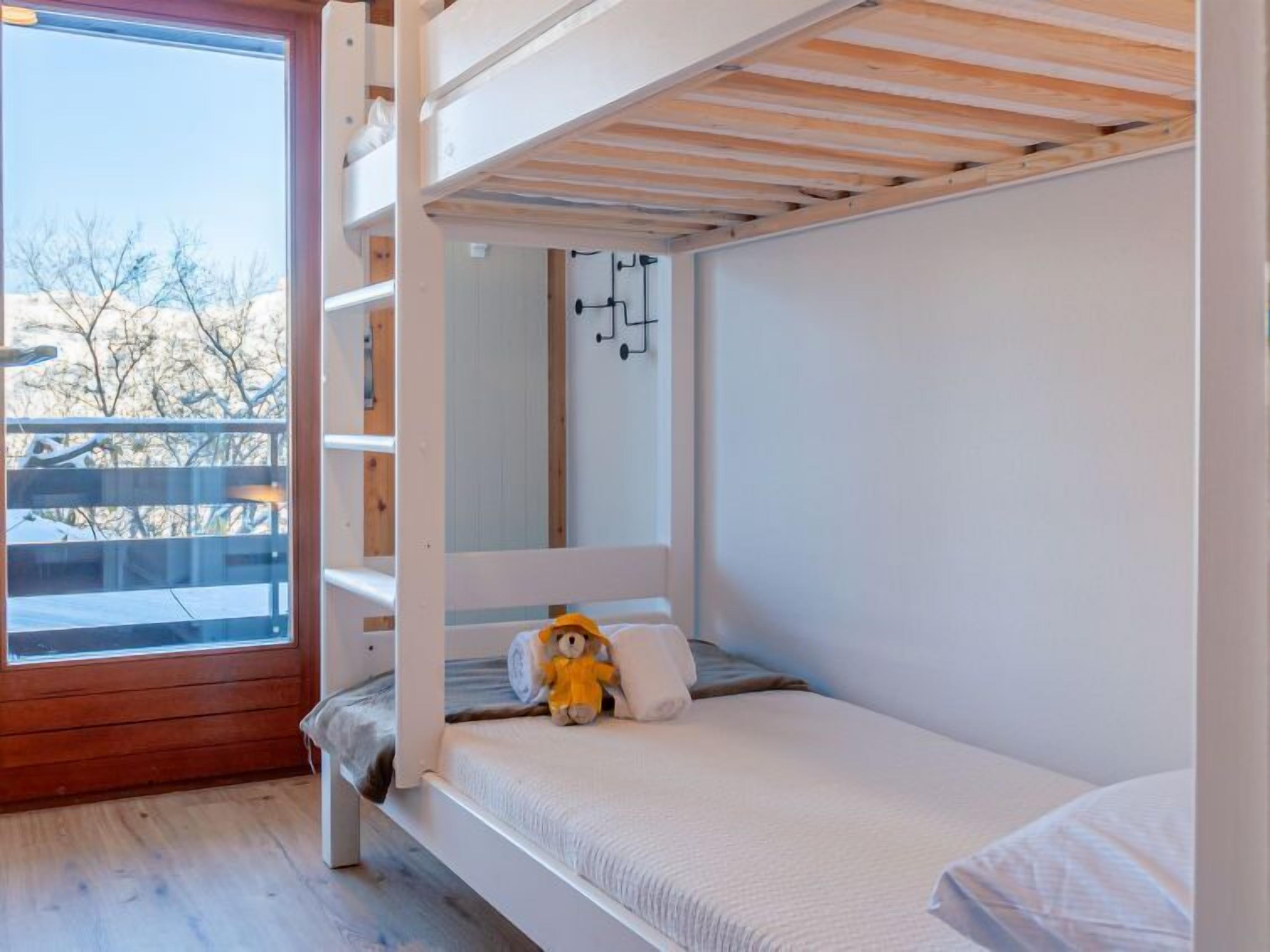 A bunk bed room with a window, a teddy bear, and a wooden deck outside.