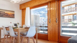 Un comedor moderno con una mesa y sillas de madera, un cuadro en la pared y un ventanal con vistas a un paisaje montañoso.