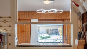 Una cocina moderna con paneles de madera, un amplio ventanal con vistas a un paisaje nevado y una lámpara colgante.