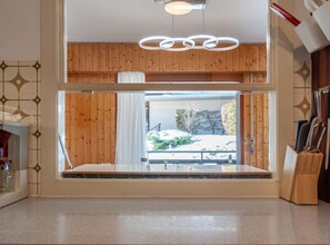 Una cocina moderna con paneles de madera, un amplio ventanal con vistas a un paisaje nevado y una lámpara colgante.