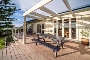 A wooden deck with a picnic table, glass doors leading to a covered patio, and a view of the landscape. - Beach Path House - Bicheno Accommodation (Bicheno)