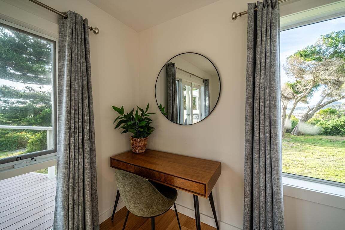 A room with a wooden desk, a round mirror, and a potted plant.