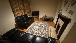 A living room with a black leather sofa, a patterned rug, a television, a small table, and a fireplace.
