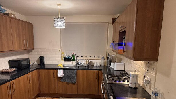 A modern kitchen with wooden cabinets, a black countertop, a gas stove, a microwave, and a hanging light fixture.