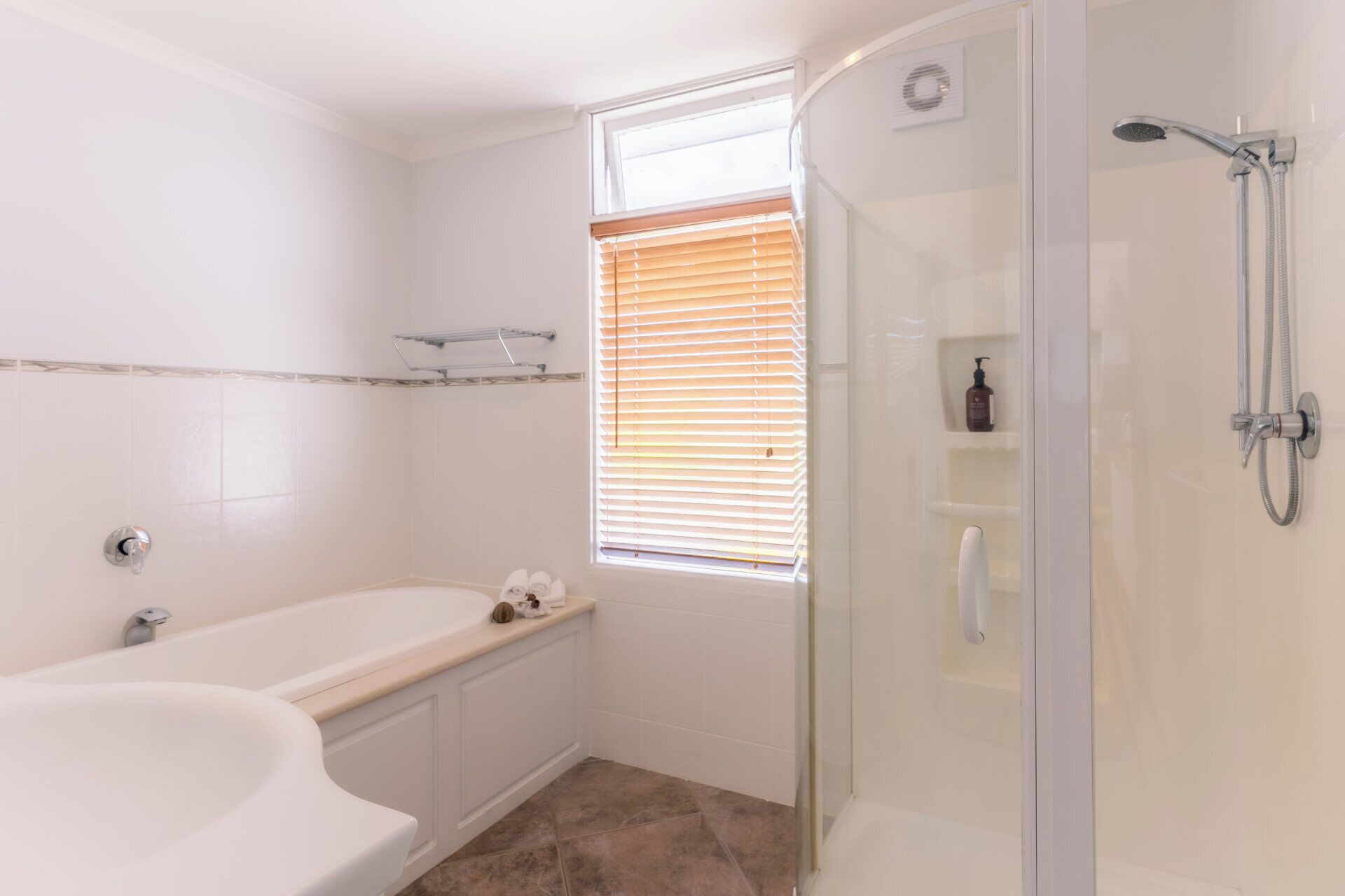Een badkamer met een bad, een douche met glazen wanden en een raam met zonwering.