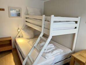 A bunk bed room with a wooden nightstand, a bedside lamp, and a framed picture on the wall.