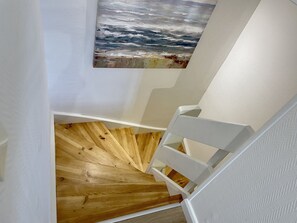 A wooden staircase with a white railing leading to a room with a textured white wall and a painting of a seascape.