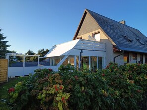 A modern house with a sloped roof, a covered patio area, and a well-maintained garden.
