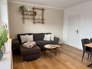 A modern living room with a grey sofa, a small round table, and a bookshelf with decorative items.