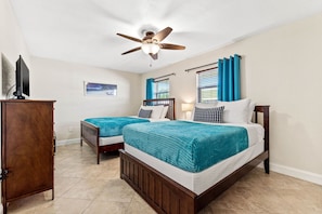 A bedroom with two beds, a ceiling fan, a TV, and a window with curtains. - Charming condo on Indian Shore beach (Indian Shores)