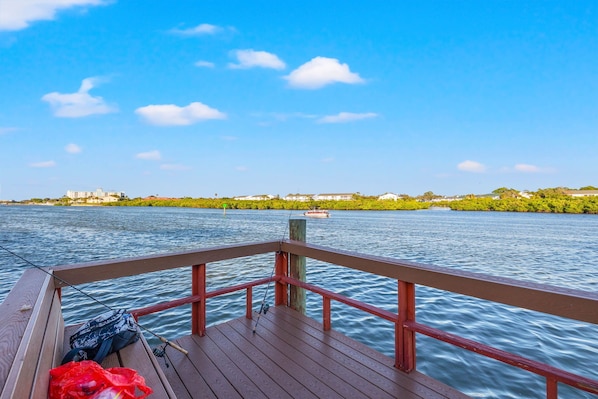 A wooden deck with a railing overlooking a calm river, with buildings and greenery in the background. - Charming condo on Indian Shore beach (Indian Shores)