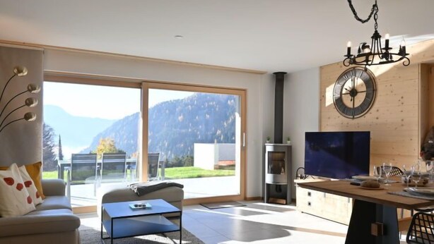 Una sala de estar moderna con un amplio ventanal corredero que da a un balcón, una chimenea y un comedor con un reloj en la pared.