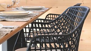 Una mesa de comedor con platos, vasos y una botella. Hay sillas negras con un diseño de celosía.