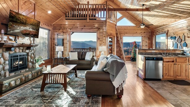 A cozy cabin interior with a fireplace, wooden furniture, a kitchen area, and a balcony with a view. - Amazing Mtn views/Hot tub/Fireplace/Bunk beds/Arcade games (Sevierville)