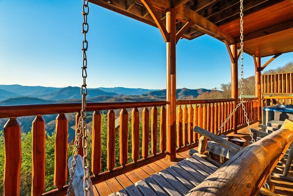 Una terraza de madera con una silla mecedora y vistas a un paisaje montañoso.