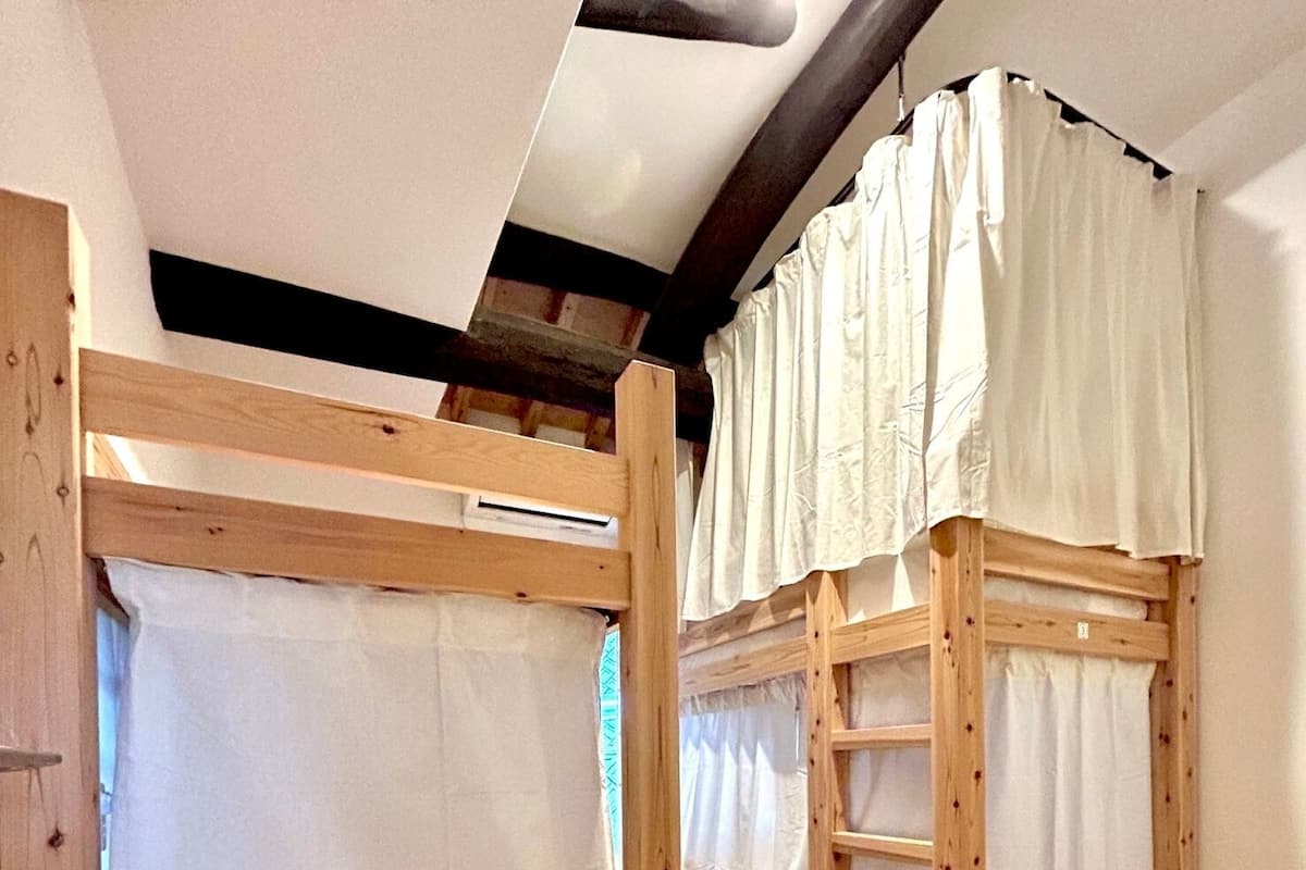 Two bunk beds with wooden frames and white bedding, in a room with wooden flooring and a sloped ceiling.