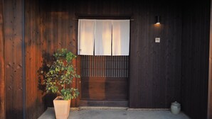 A wooden entrance with a potted plant, a sliding door, and a small trash can. - KOTOBUKIAN (Awaji)