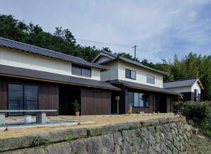 A traditional Japanese house with a tiled roof, wooden exterior, and a stone retaining wall. - KOTOBUKIAN (Awaji)