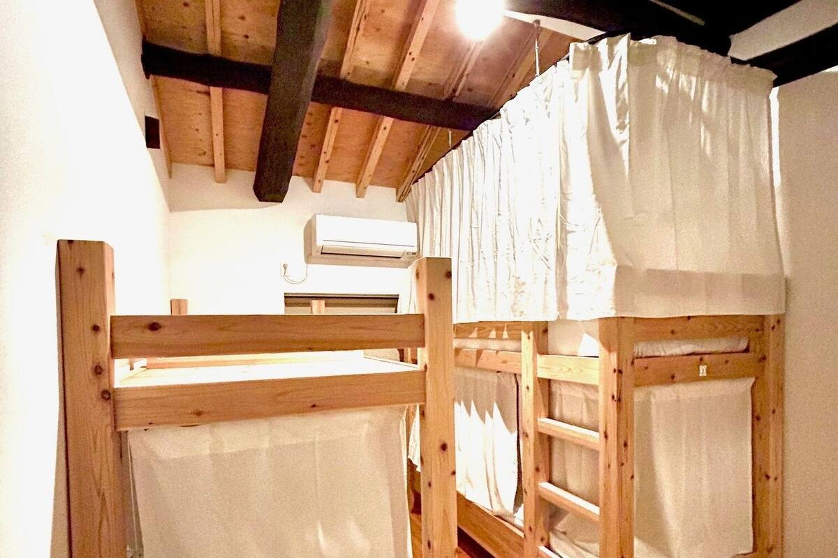 Two wooden bunk beds with white sheets, a ceiling fan, and an air conditioning unit in a room with wooden flooring.