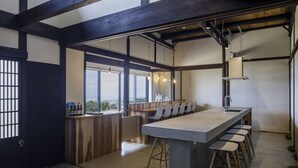 A modern kitchen with a large island, bar stools, and a view through large windows. - KOTOBUKIAN (Awaji)