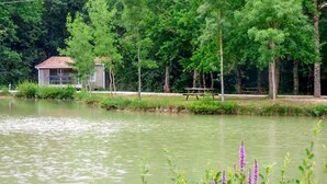 A lakeside view with a small house, a picnic table, and dense greenery. - Amazing (sta)caravan in CHEF-BOUTONNE (CHEF-BOUTONNE)