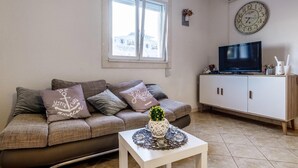 Un salon avec un canapé, une petite table sur laquelle est posé un vase, un téléviseur sur un meuble et une horloge au mur.