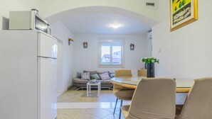 Un espace de vie compact comprenant un coin cuisine, un espace repas avec une table en verre et un canapé avec des coussins.