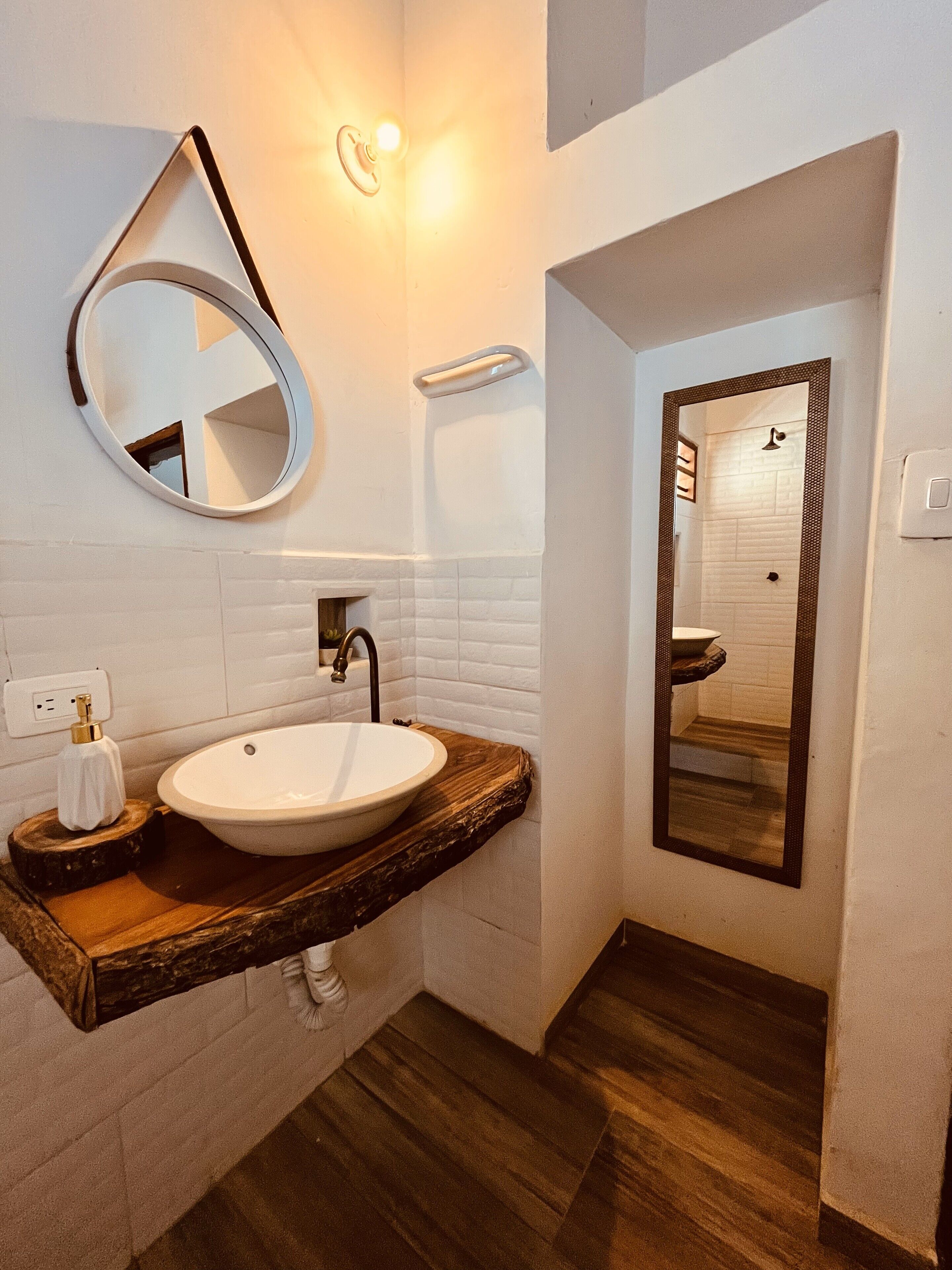 A bathroom with a white sink, wooden countertop, and a round mirror.