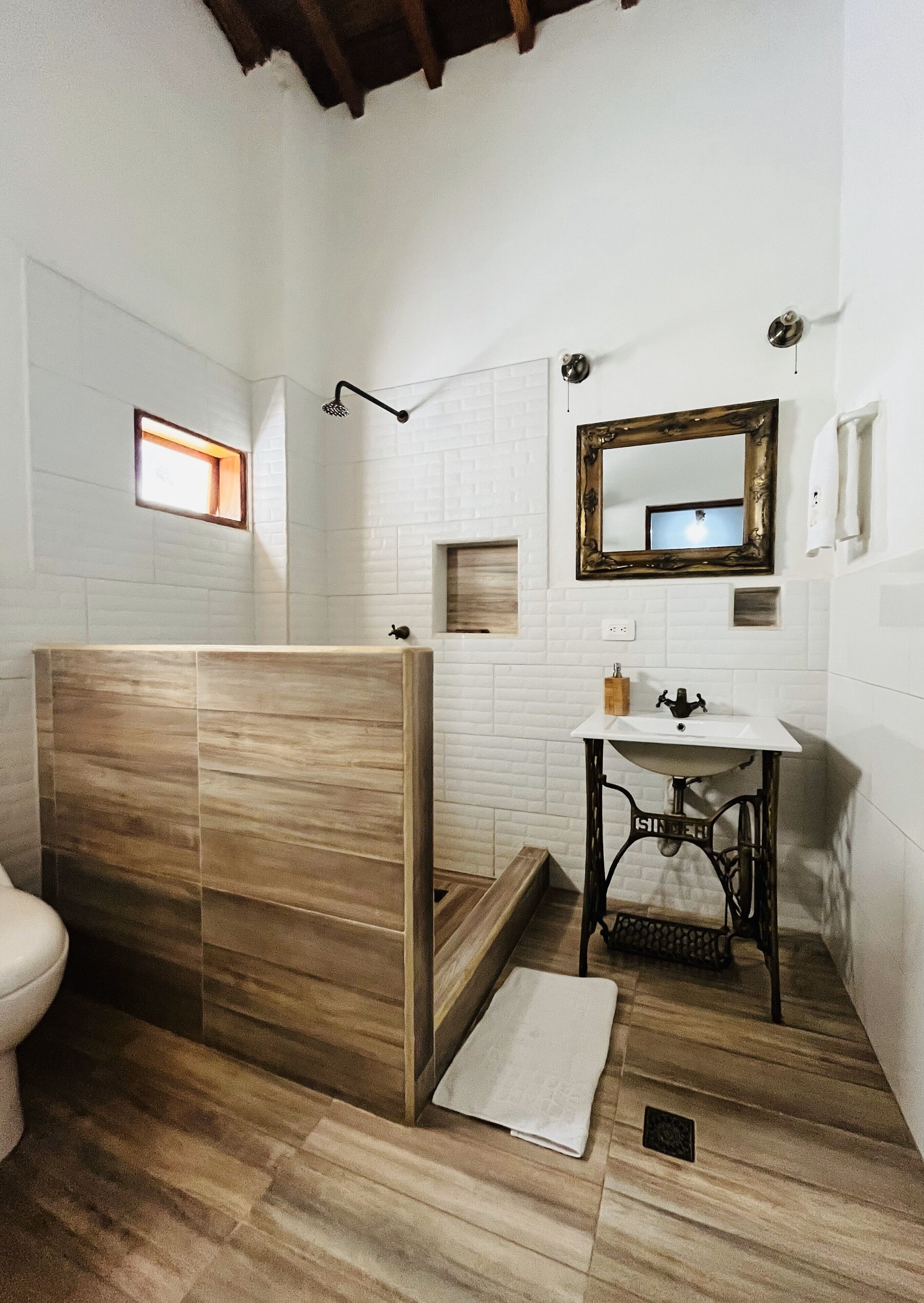 A bathroom with a wooden shower enclosure, a sink with a vintage-style mirror, and a small window providing natural light.