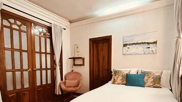 Un dormitorio con cama, una silla, ventilador de techo, una puerta y un cuadro en la pared.