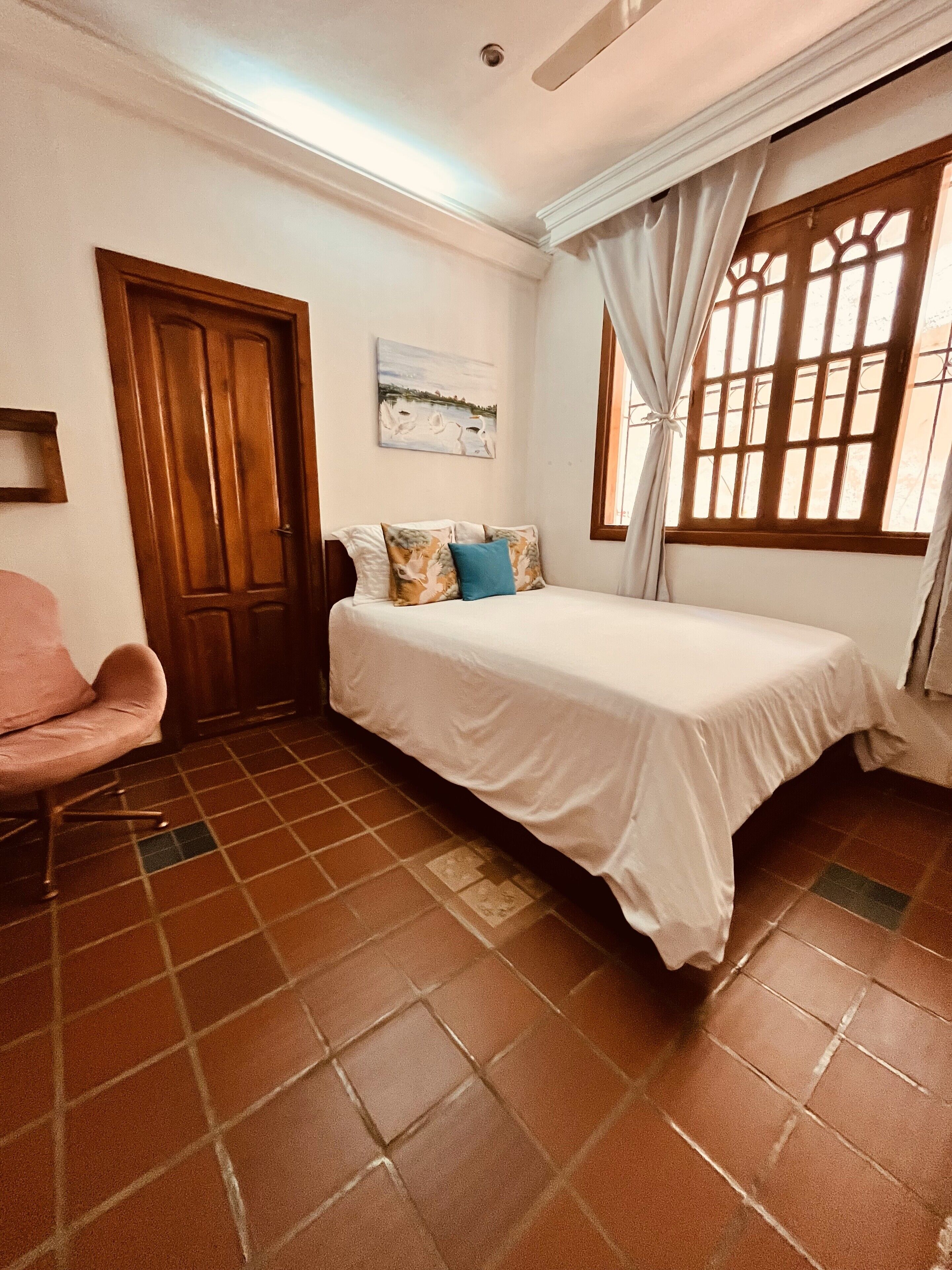 A bedroom with a bed, a chair, a door, and a window with curtains.