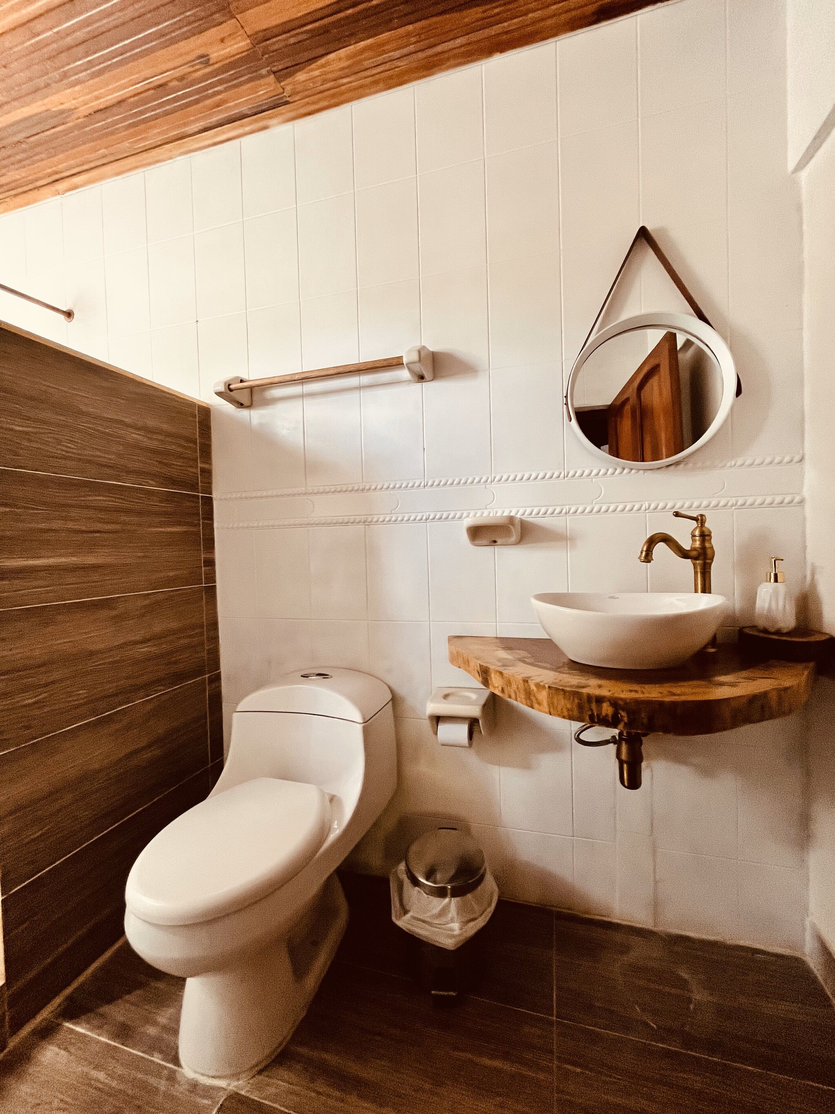 A modern bathroom with a wooden vanity, a round mirror, and a white toilet.