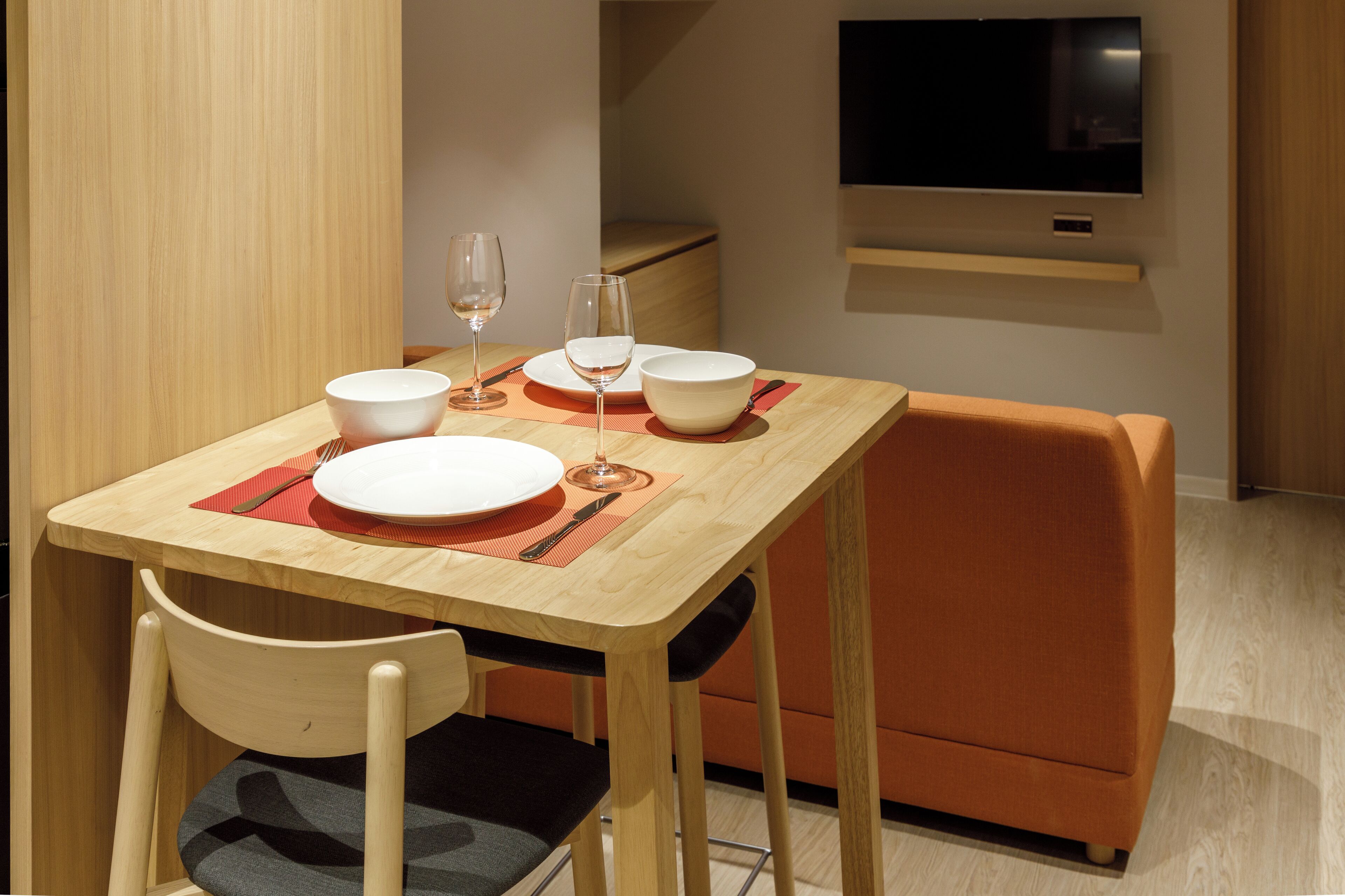 A dining area with a wooden table, two chairs, and a flat-screen TV mounted on the wall.