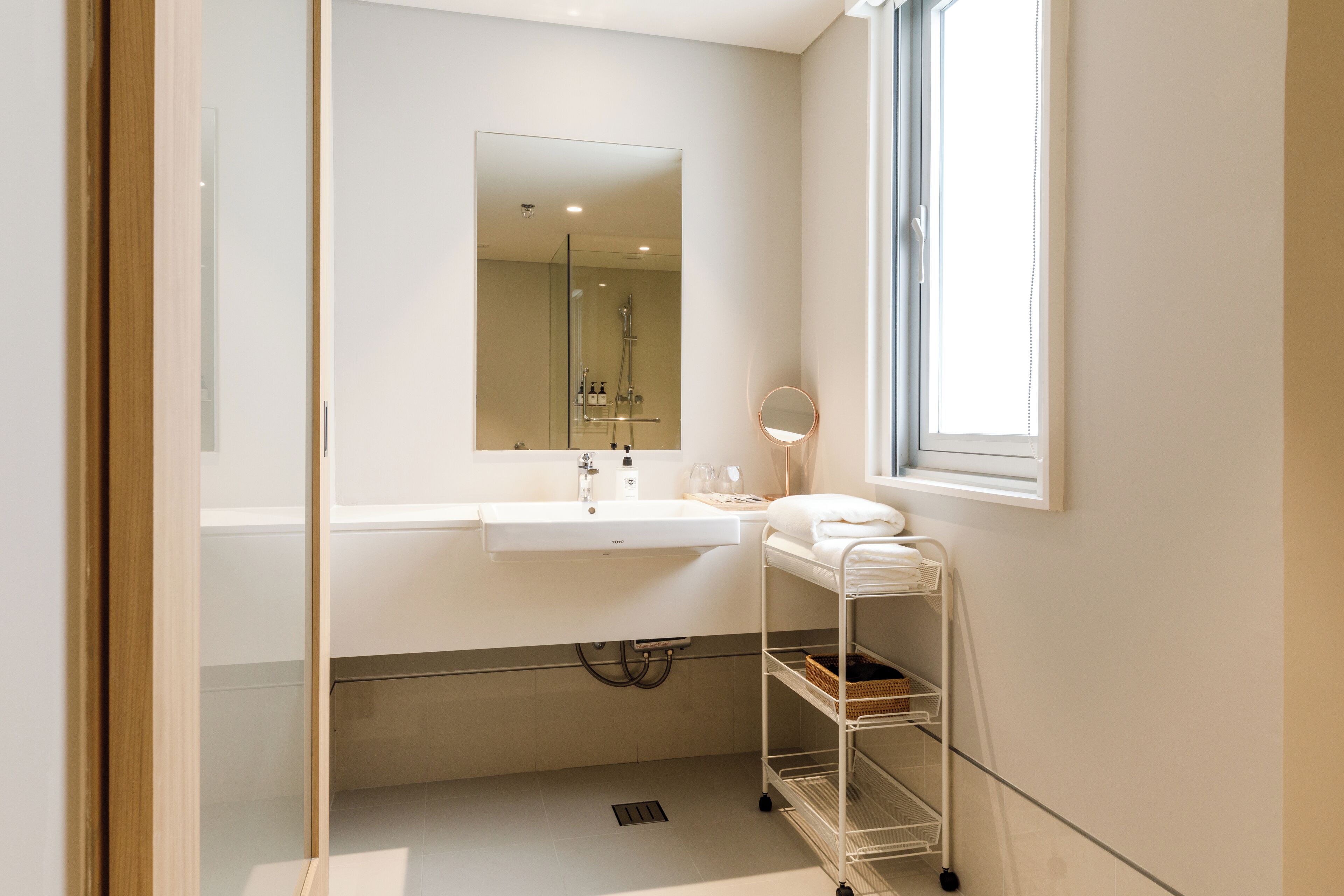 A modern bathroom with a white sink, mirror, and a window providing natural light.