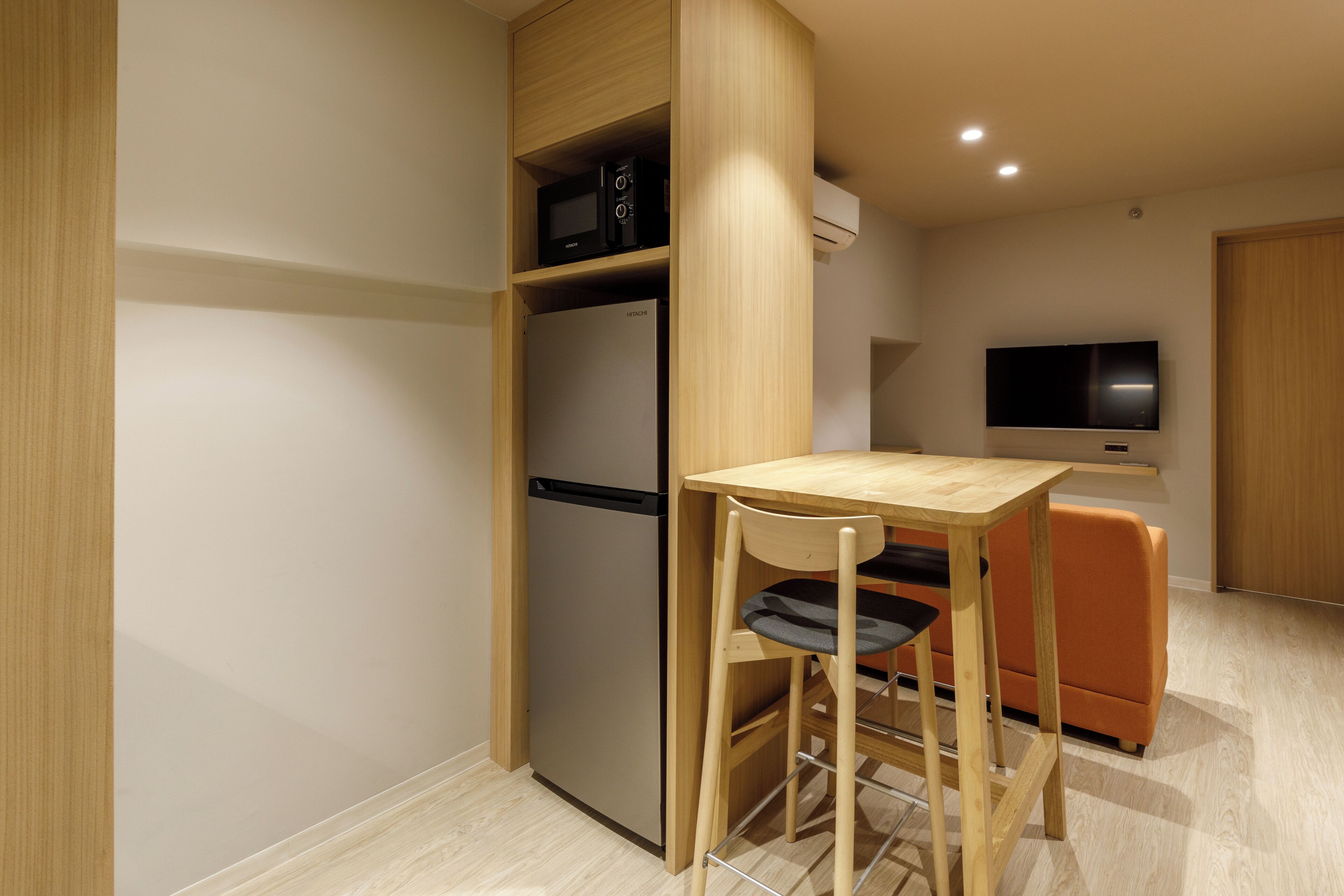 A compact kitchen with a built-in microwave, a refrigerator, and a flat-screen TV mounted on the wall.