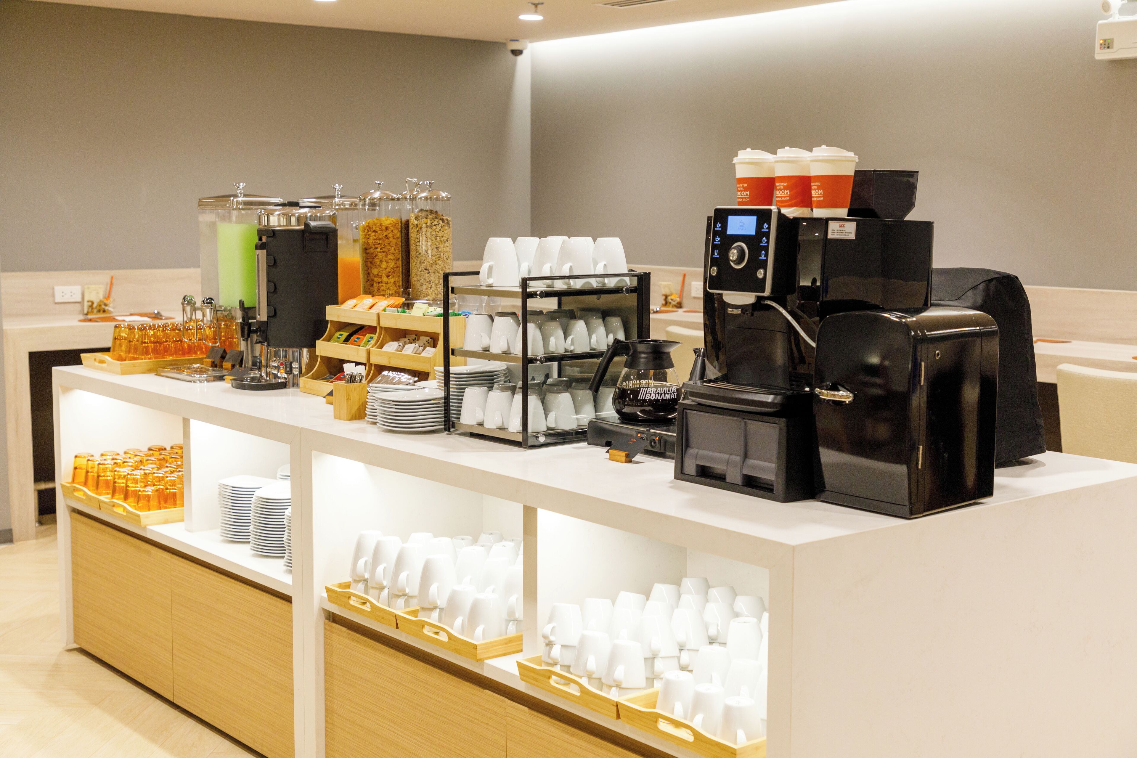 Una estación de café con varias máquinas de café, un dispensador de bebidas y una variedad de tazas y recipientes.