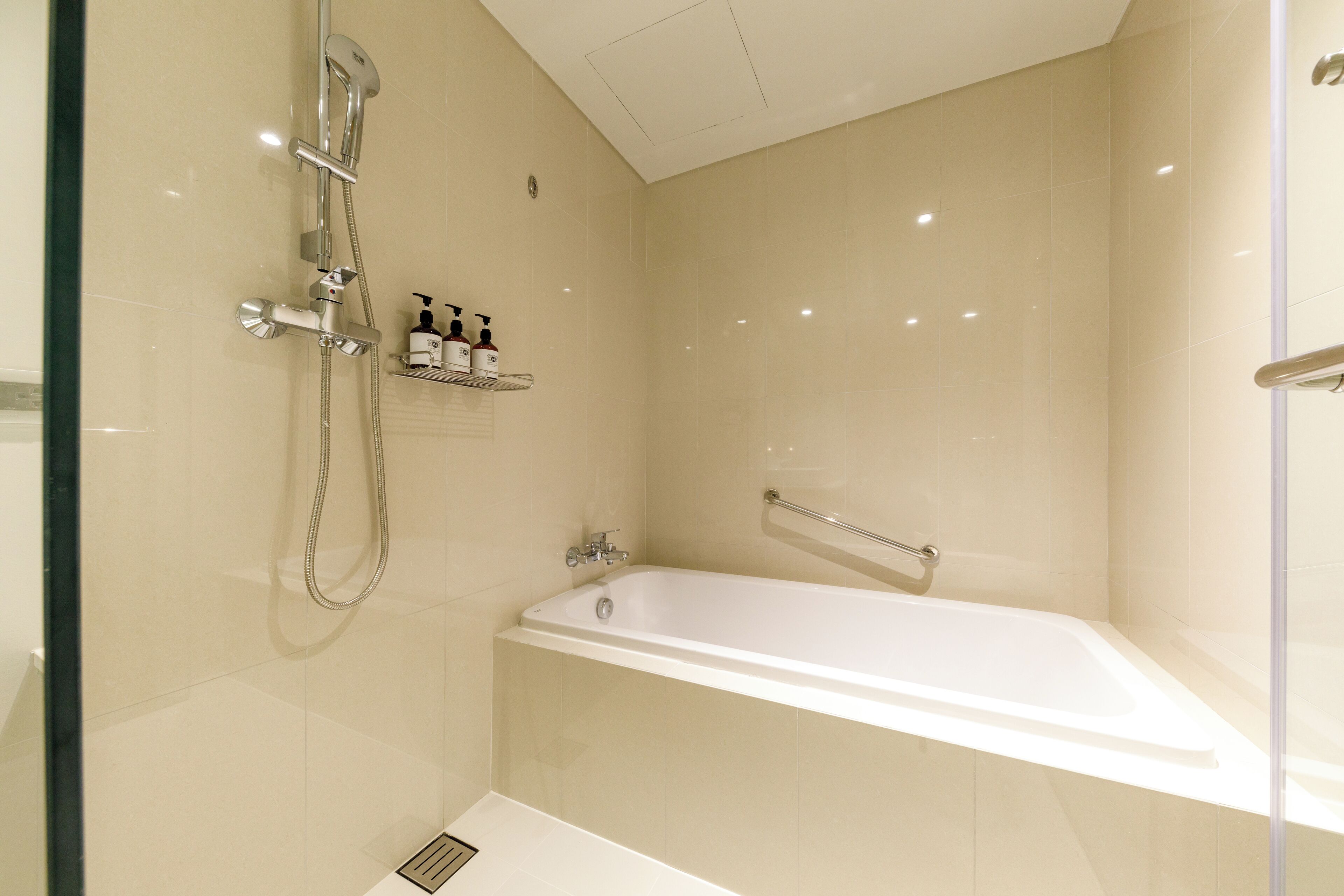 Et moderne badeværelse med bruseniche, et hvidt badekar og en hylde med toiletartikler.
