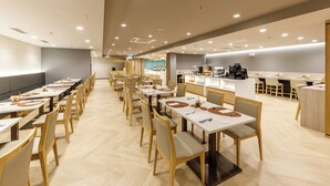 A spacious dining area with long tables and chairs, a kitchen area with a coffee machine, and a counter with a menu display. - Nishitetsu Hotel Croom Bangkok Silom (Bangkok)