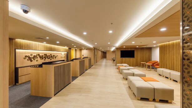 A hotel reception area with a wooden reception desk, a wall-mounted TV, and a seating area with cushioned benches. - Nishitetsu Hotel Croom Bangkok Silom (Bangkok)