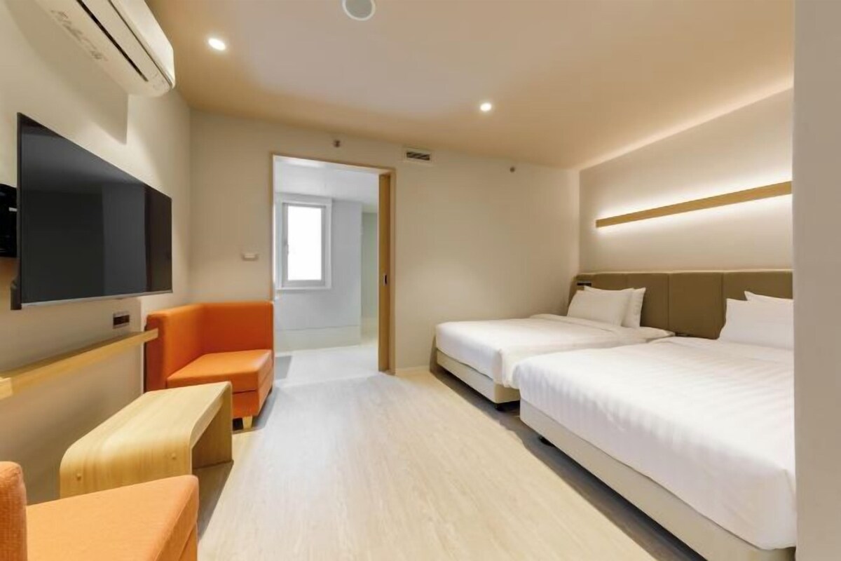 A hotel room with a TV, two beds, a sofa, and a wooden bench.
