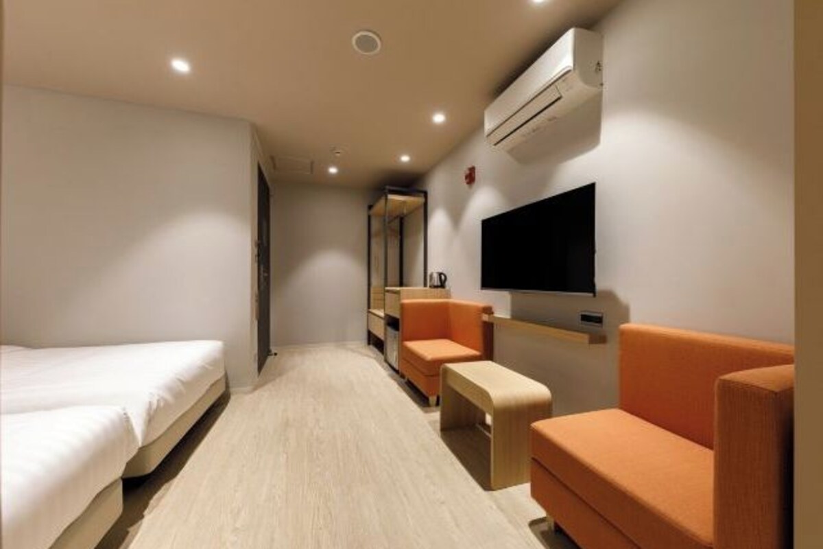 A hotel room with a bed, a sofa, a small table, and a TV mounted on the wall.