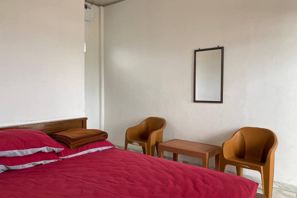 Ein schlichtes Zimmer mit einem Bett, zwei Stühlen, einem kleinen Tisch und einem Spiegel an der Wand.