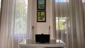 A room with sheer curtains, a glass display case, and three framed pictures on the wall.