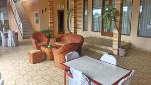 A covered outdoor seating area with wicker furniture, a table, and potted plants.